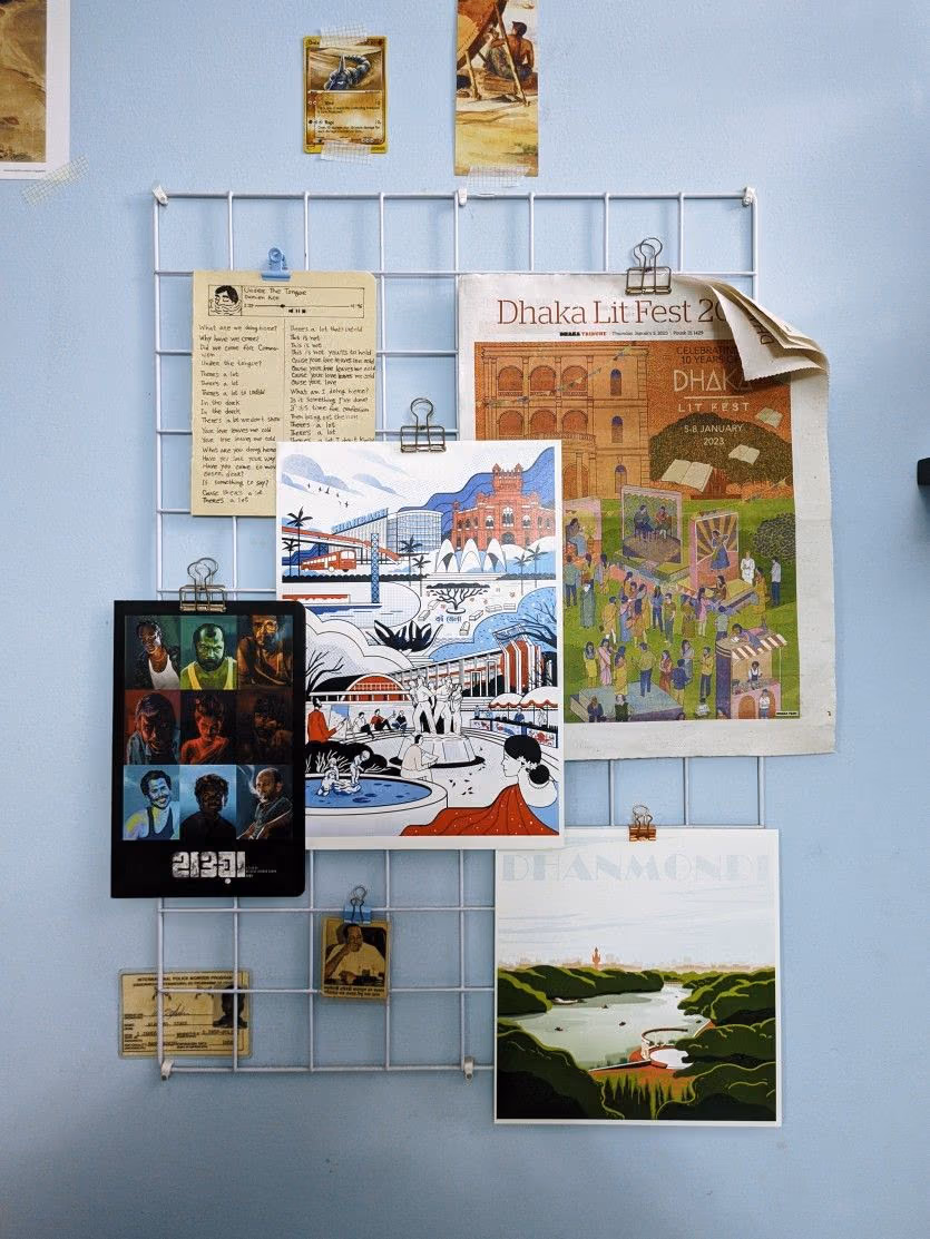 A white wire grid panel with clipped notes and prints on a pale blue wall.